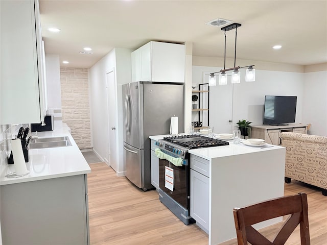 kitchen featuring stainless steel appliances, light countertops, light wood finished floors, a sink, and visible vents