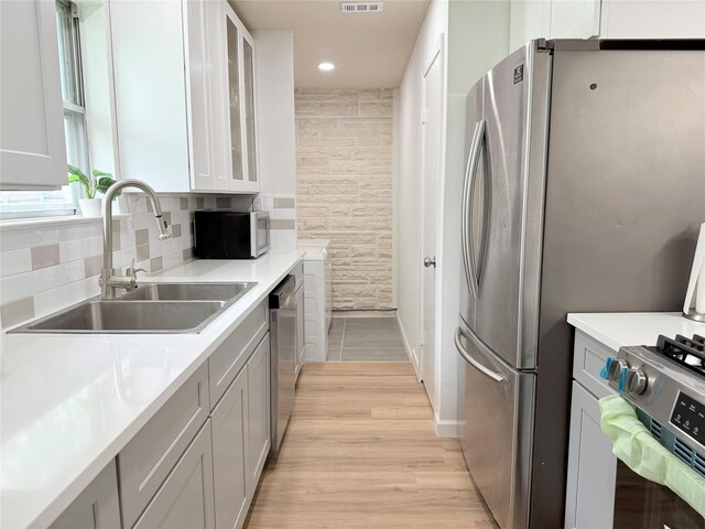 kitchen with glass insert cabinets, decorative backsplash, light wood-style floors, appliances with stainless steel finishes, and a sink