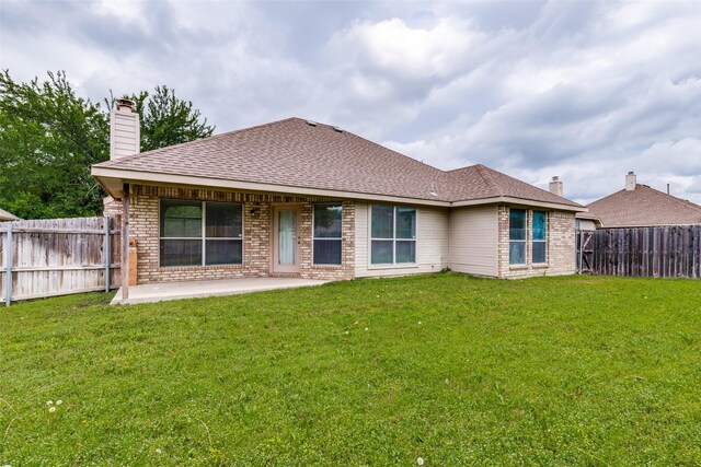 back of property featuring a chimney, brick siding, a fenced backyard, a yard, and a patio