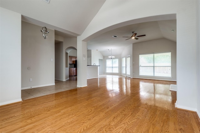 unfurnished living room with a ceiling fan, arched walkways, wood finished floors, and lofted ceiling