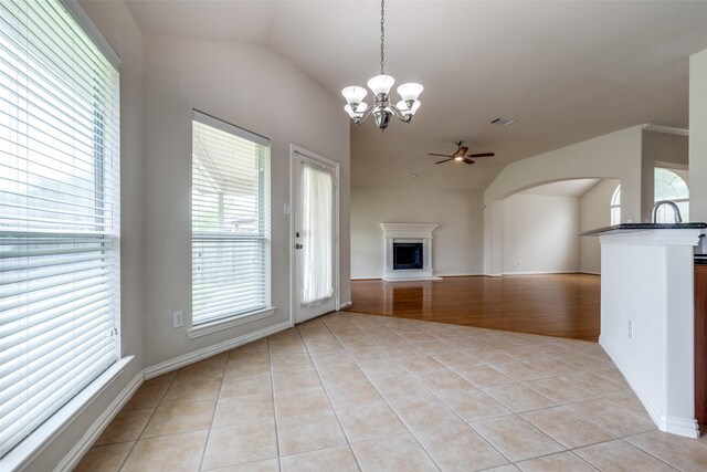 unfurnished living room with a fireplace with raised hearth, vaulted ceiling, light tile patterned floors, and ceiling fan with notable chandelier
