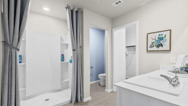 full bath featuring a sink, a shower stall, visible vents, baseboards, and wood finished floors