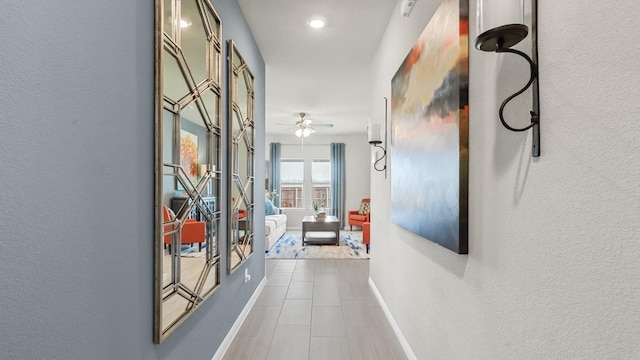 hallway featuring baseboards, tile patterned flooring, and a textured wall