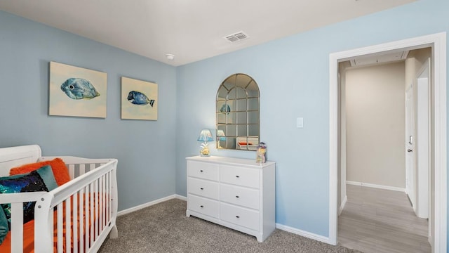bedroom featuring a crib, visible vents, light colored carpet, and baseboards