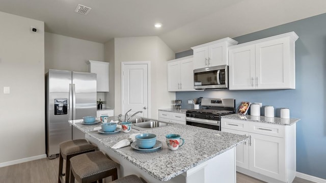 kitchen with light wood finished floors, a sink, stainless steel appliances, a breakfast bar area, and baseboards