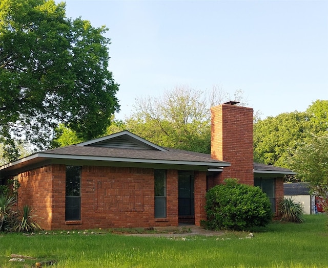 back of property with a chimney, brick siding, a yard, and roof with shingles