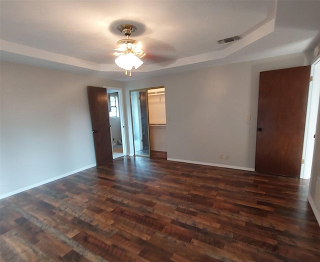 unfurnished room featuring a raised ceiling, visible vents, baseboards, dark wood finished floors, and a ceiling fan