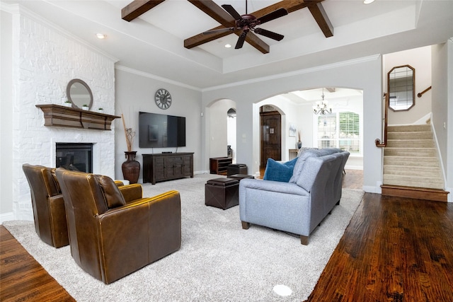living room with arched walkways, wood finished floors, a stone fireplace, baseboards, and stairway