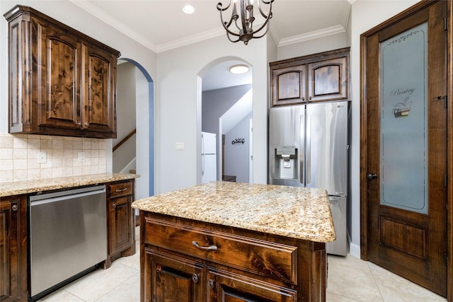 kitchen with light tile patterned floors, light stone counters, arched walkways, and appliances with stainless steel finishes