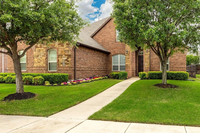 obstructed view of property with roof with shingles, brick siding, and a front lawn