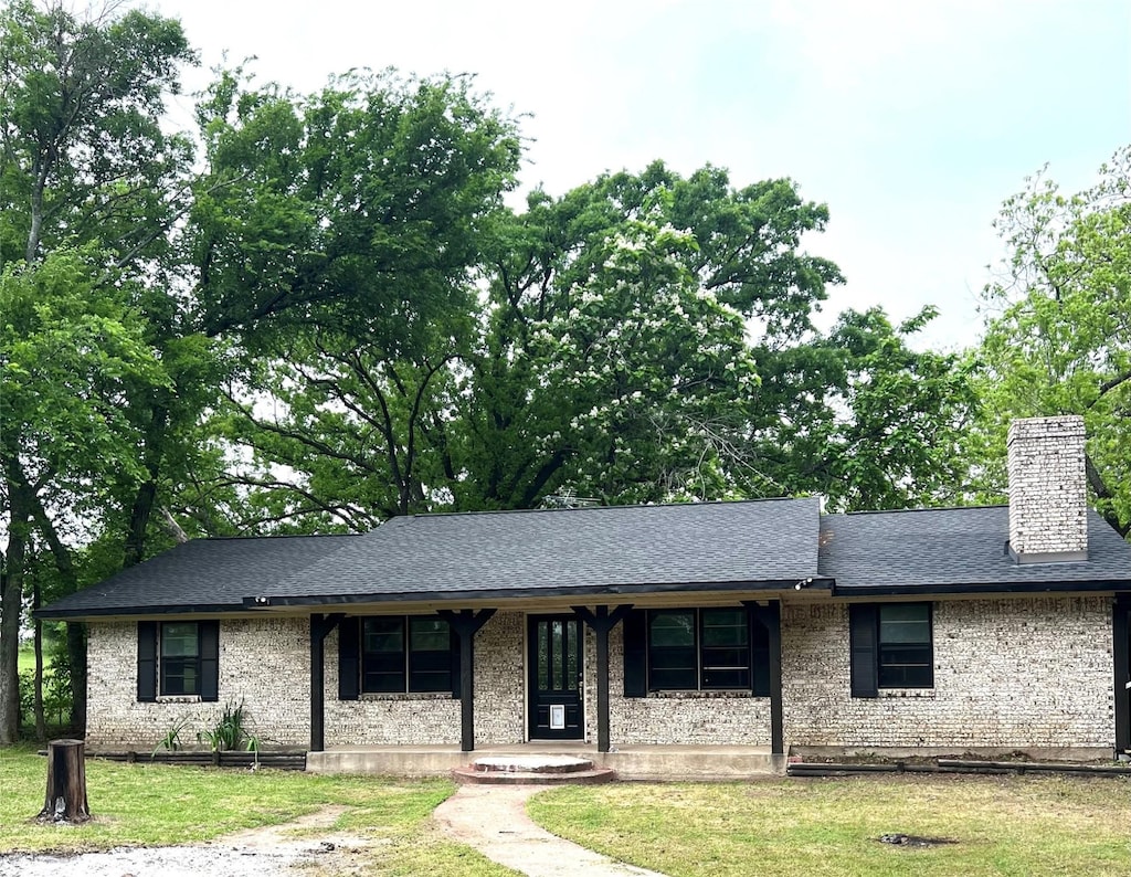 ranch-style home featuring a shingled roof, a chimney, a porch, and a front lawn