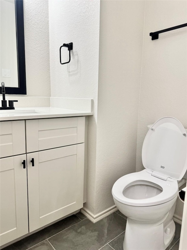 half bath with vanity, a textured wall, toilet, and tile patterned floors