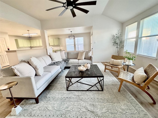 living area featuring lofted ceiling, light wood-style flooring, and ceiling fan with notable chandelier