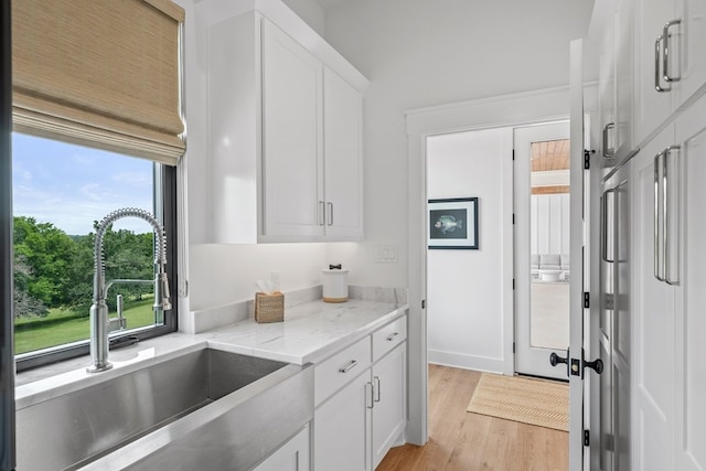kitchen with a sink, white cabinetry, light wood-style flooring, and light stone countertops