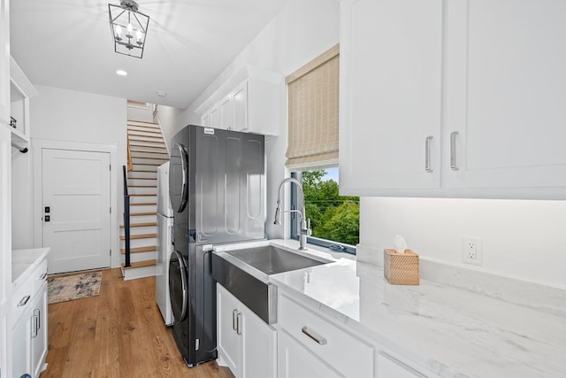 laundry room featuring stacked washer / drying machine, cabinet space, a sink, light wood-style floors, and recessed lighting