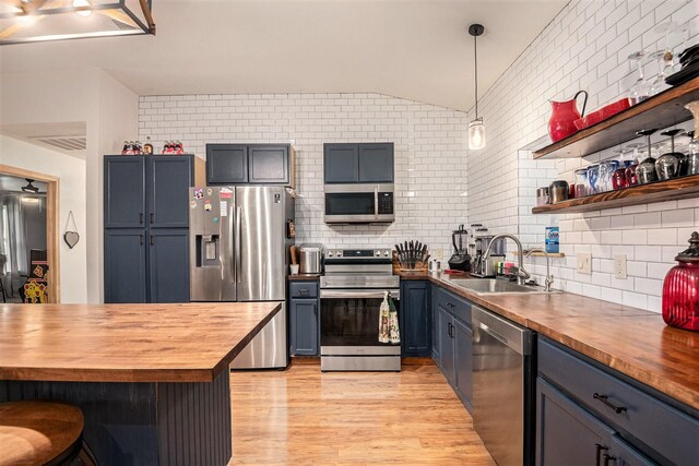 kitchen with a sink, light wood-style floors, wood counters, stainless steel appliances, and tasteful backsplash