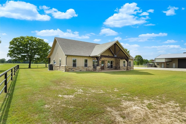exterior space with fence, stone siding, roof with shingles, central air condition unit, and a yard