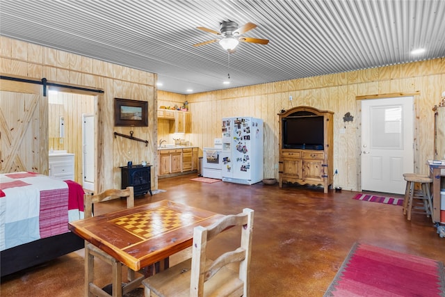 living room with concrete flooring, ceiling fan, wood walls, and a wood stove