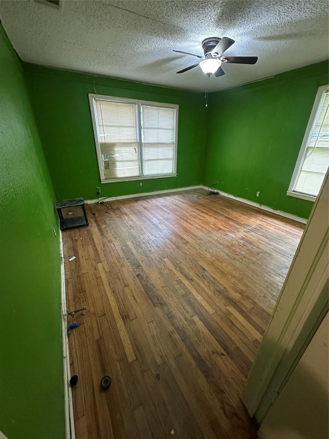 unfurnished room with a textured ceiling, ceiling fan, hardwood / wood-style floors, and a wealth of natural light