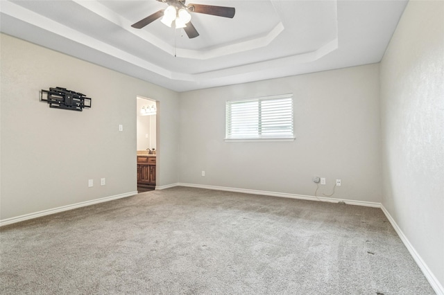 carpeted empty room with a ceiling fan, baseboards, and a raised ceiling