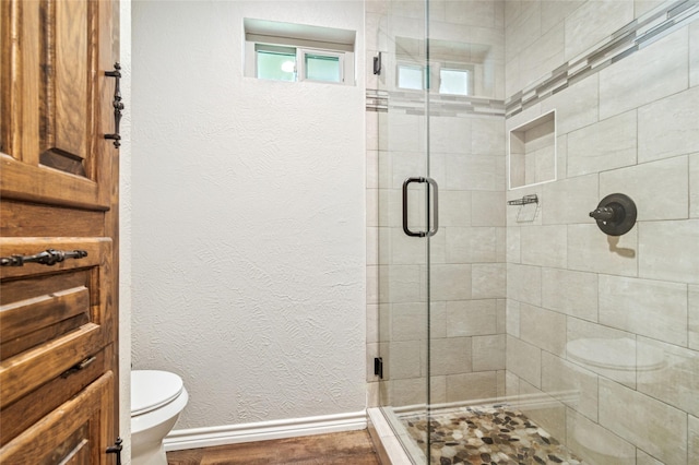 full bath featuring baseboards, a stall shower, toilet, and wood finished floors