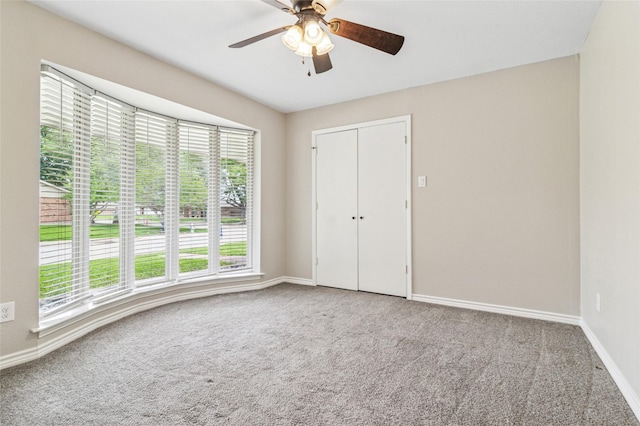unfurnished bedroom with baseboards, ceiling fan, carpet, and a closet