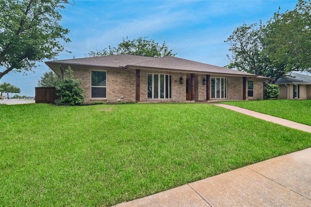 single story home featuring brick siding, a front yard, and roof with shingles