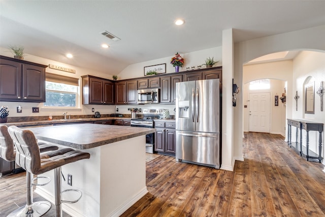 kitchen featuring visible vents, dark brown cabinetry, arched walkways, dark wood finished floors, and stainless steel appliances