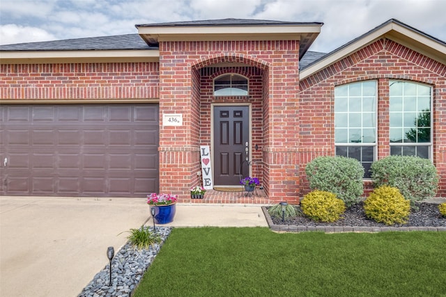 doorway to property featuring a garage, driveway, roof with shingles, and brick siding