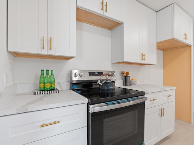 kitchen featuring stainless steel range with electric stovetop, light tile patterned flooring, light stone countertops, and white cabinetry