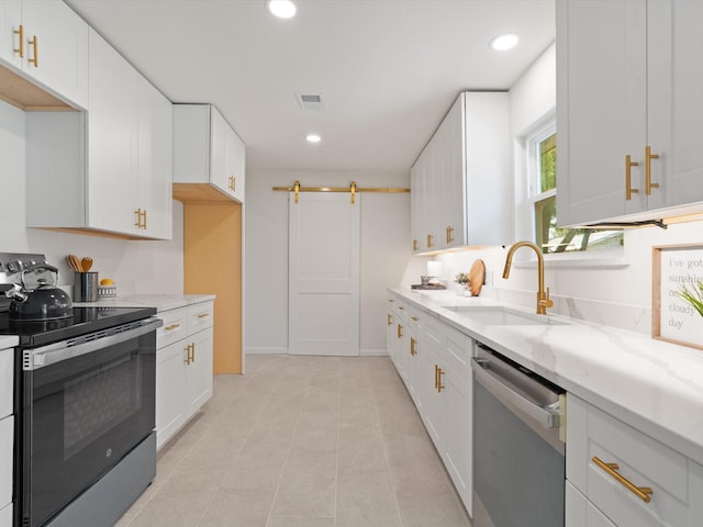 kitchen with light stone countertops, appliances with stainless steel finishes, a barn door, a sink, and visible vents