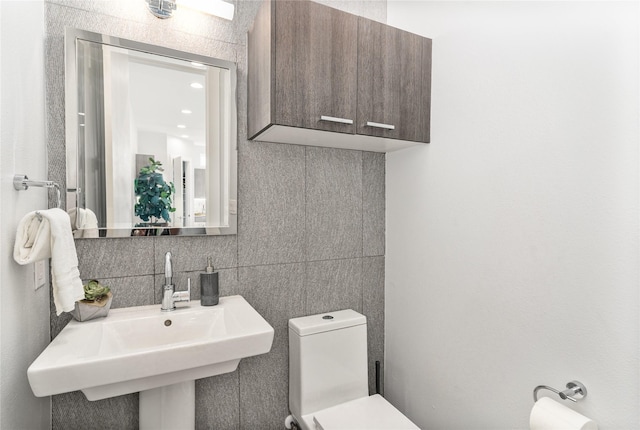 half bathroom with a sink, backsplash, toilet, and tile walls
