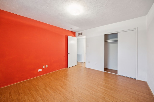 unfurnished bedroom with a textured ceiling, a closet, wood finished floors, and visible vents