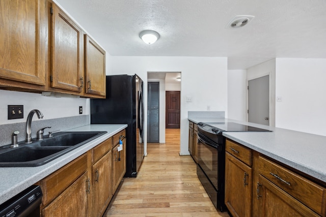 kitchen with brown cabinetry, a sink, light wood-style flooring, and black appliances