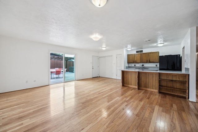 kitchen with visible vents, brown cabinets, light wood-type flooring, light countertops, and open floor plan