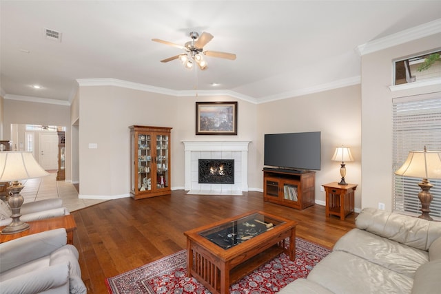 living room featuring ceiling fan, visible vents, a tile fireplace, wood finished floors, and baseboards