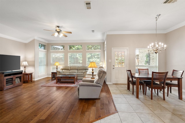 living room featuring visible vents, light wood-type flooring, baseboards, ceiling fan with notable chandelier, and ornamental molding