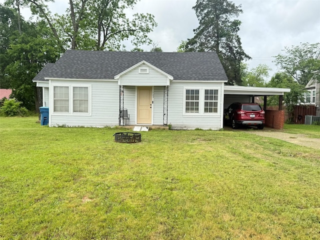 view of front of house with a fire pit, a front yard, roof with shingles, an attached carport, and driveway