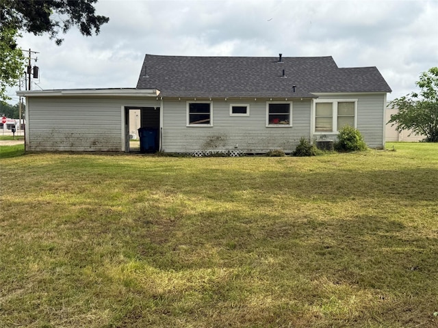 rear view of property featuring a shingled roof and a yard