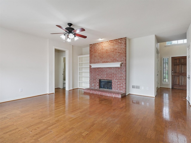unfurnished living room with ceiling fan, a brick fireplace, baseboards, wood finished floors, and visible vents
