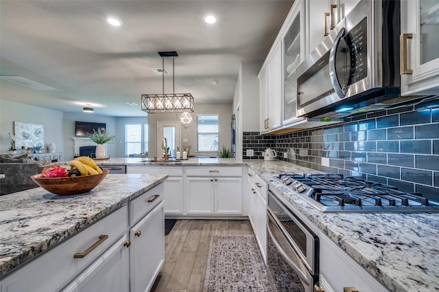 kitchen featuring a peninsula, open floor plan, white cabinets, a sink, and stainless steel appliances