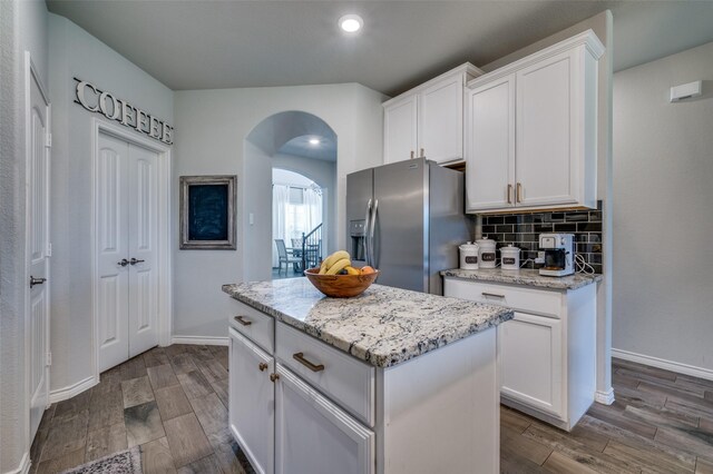 kitchen featuring backsplash, a kitchen island, stainless steel refrigerator with ice dispenser, arched walkways, and white cabinets
