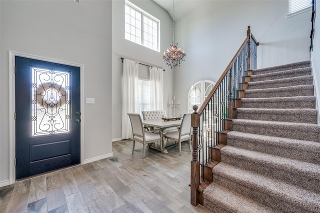 foyer entrance with a high ceiling, a notable chandelier, light wood-style flooring, stairs, and baseboards