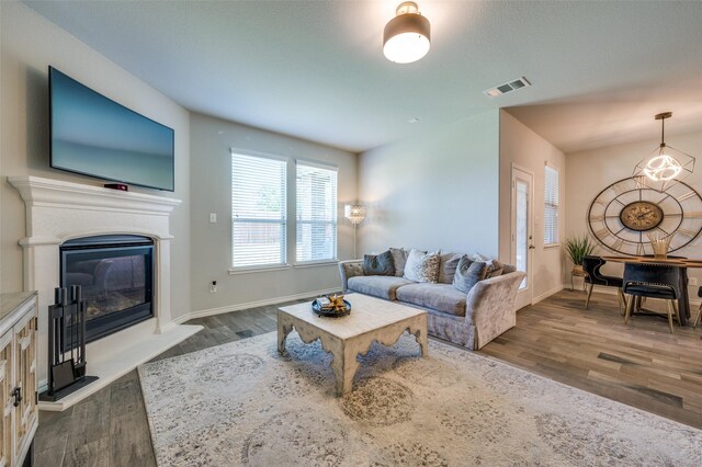 living area with baseboards, visible vents, a glass covered fireplace, and dark wood-type flooring