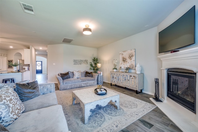 living room with arched walkways, visible vents, a glass covered fireplace, and dark wood finished floors