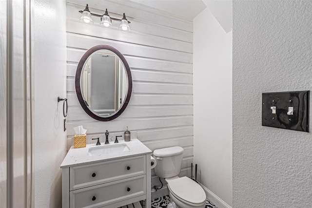 half bath featuring vanity, a textured wall, and toilet