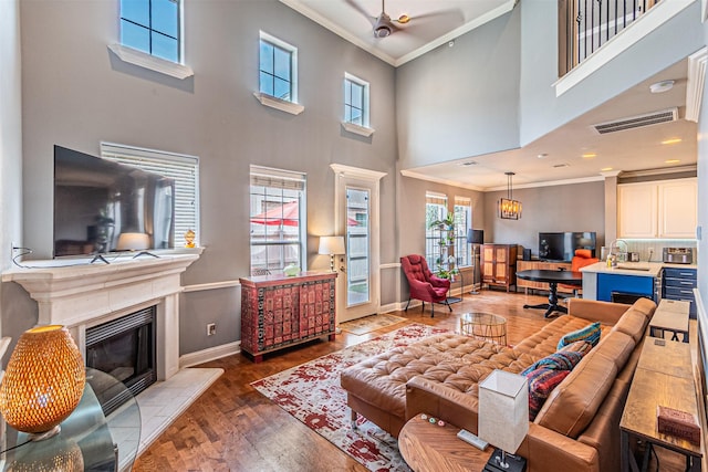 living room with a healthy amount of sunlight, visible vents, crown molding, baseboards, and a high ceiling
