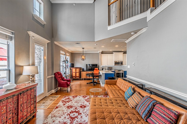 living area with crown molding, a high ceiling, baseboards, and light wood-style floors