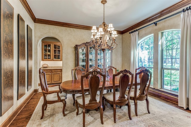 dining room featuring an inviting chandelier, baseboards, crown molding, and wood finished floors