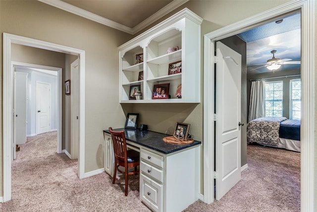 office area featuring a ceiling fan, light colored carpet, built in desk, baseboards, and ornamental molding